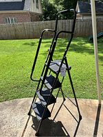 Full view of the large black step ladder showing four steps, tubular frame and safety handrails.