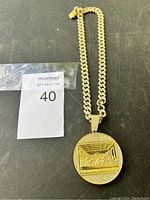 Gold tone curb chain necklace with round pendant showing The Last Supper design surrounded by rhinestones.