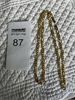 Gold chain necklace laid out on white quilted fabric alongside MaxSold lot number card showing number 87.
