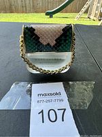 Perfume bottle with snake-skin patterned cap and gold chain handle displayed outdoors on a table with grassy backyard in background.