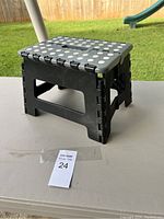 Small collapsing stool shown from top angle on outdoor table with visible handle and grip dots