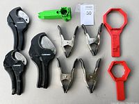 Photo showing three black Husky pipe cutters, four metal spring clamps, and two red plastic pipe wrenches laid out on white surface.
