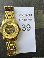 Full view of gold-tone Tevise skeleton watch on bracelet beside MaxSold lot number paper.