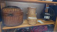 Photo showing three woven baskets and a black spherical metal candle holder with a white candle inside displayed on a wooden shelf.