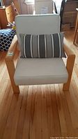 Front view of wooden framed chair with light fabric cushions and striped pillow on seat.