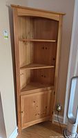 Front view of the pine corner cabinet showing the three shelves and the lower cabinet door.