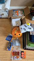 Overview photo of Halloween decoration lot, showing jack-o'-lantern pumpkin, clown costume pieces, spider webs, string lights, and various small decor items on floor.