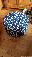 Front view of round blue and white patterned stuffed hassock on wood floor