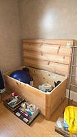 Open wooden storage chest containing household items such as an exercise ball and boxes, showing the general condition and interior.
