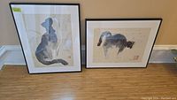 Two framed cat-themed prints, one with cat sitting silhouette and the other cat stretching, both with artist signature and Asian-style red stamp