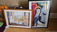 Two framed prints side by side, one with a window view and another with an abstract face