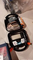 Image of Black & Decker Mouse sander and assortment of sanding pads inside black carrying case, displayed on surface.