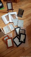 Overview of assorted frames including easel, small wooden, plastic, and matting boards spread on floor.
