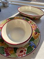 Three ceramic serving dishes with cream backgrounds and colorful floral patterns on rims, red trim edges visible.