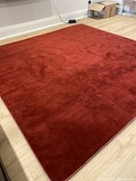 Photo showing the full red rug laid on light wood flooring, displaying its rich color and texture.