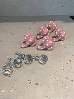 Set of five pink ceramic elephant-shaped knobs with white polka dots and four clear faceted plastic ball knobs on table surface.