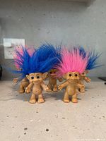 Five original troll dolls arranged in an arc, showing bright blue and pink hair colors, standing on a grey speckled countertop.