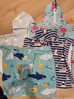 Four children's hooded towels each with unique colorful aquatic or flamingo patterns, folded and laid on a wooden surface.