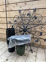 Assortment of black plastic plant pots in two stacks, green nursery pot, black decorative metal garden ornament with ornate floral design and damage to tip.