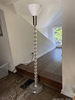 Full view of the tall floor lamp showing its metal base, glass ball stack stand, white cone-shaped lampshade, and electrical cord on hardwood floor.