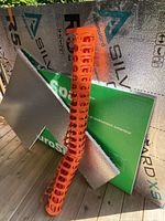 Three construction materials leaning against a wooden surface: silver reflective board, green foam board, orange safety fence.
