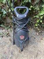 Front view of Jobmate 1500psi electric pressure washer showing front logo, hose and power cord wrapped around body, handle on top, and cracked/missing bottom portion.