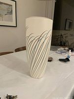 Front and side view of John Bergen ceramic vase with painted grass pattern on cream base, displayed on a white table.