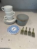 Espresso cups stacked on saucers, butter dish, coaster with Cuervo branding, four small forks used as cheese markers.