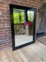 Photo showing the full mirror standing against a brick wall outside with visible reflection of outdoor scenery.