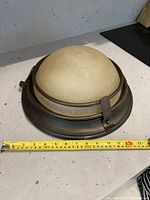 Full view of the beige glass dome pendant light with metal frame, placed on countertop with measuring tape showing approx. 12-inch diameter.