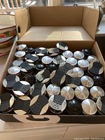 Box of over 40 glass spice jars with silver lids and black plastic flip tops, arranged tightly in a box, overhead view showing majority of lids have a flip shaker cover.