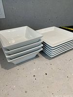Four stacked square cereal bowls alongside six stacked square salad plates all in white ceramic.