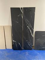 Two tall black rectangular tile cutoffs standing upright showing white veining patterns on black background, with beige tiles partially visible on side.