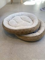 Two stacked round animal beds, tan with cream plush inner cushion visible.