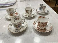 Six porcelain demitasse espresso cups and saucers with floral designs and scalloped edges, some with gold rim wear.