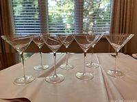 Seven clear martini glasses with long stems arranged in a line, showing their classic shape.