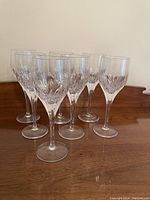 Seven clear crystal wine glasses arranged on a wooden surface, showing diamond cut pattern detail.