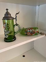 Photo showing both green glass beer stein with ornate metal lid and matching glass horn with cord.