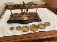 Front view of brass scale with wooden base and seven brass weights arranged in front.