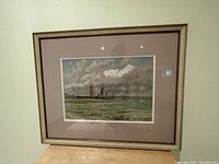 Framed print showing sailboats on a water body under a cloudy sky with green water in foreground, beige mat and thin gold frame.