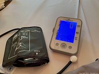 Digital blood pressure monitor with blue backlit display and left arm cuff placed on white surface.