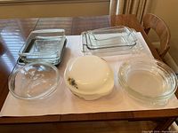 Six bakeware pieces displayed on table: multiple clear glass casserole dishes and one white ceramic covered dish with fruit motif.