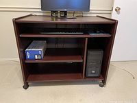 Wooden computer desk from side angle showing shelves and computer tower space with wheels.