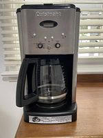 Front view of Cuisinart coffee maker showing stainless steel face, control buttons, knobs, and glass carafe.