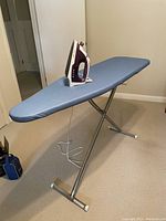 Ironing board fully extended with iron placed on it, showing blue cover and metal legs.