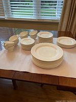 Full view of all dishes arranged on table, showing stacks of dinner plates, medium plates, salad plates, tea cups, and saucers.