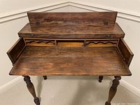 Front view of open antique wooden desk with fold-down writing surface showing internal compartments