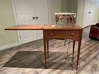 Vintage Singer sewing machine mounted in wooden cabinet with fold-out extension side surface and knee pedal under-table