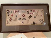 Framed petit point sampler with multiple small stitched motifs on woven canvas, dark wooden frame.