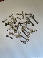 Photo showing 29 petite antique metal keys with various bow shapes, sizes, and shaft lengths arranged on a white surface.